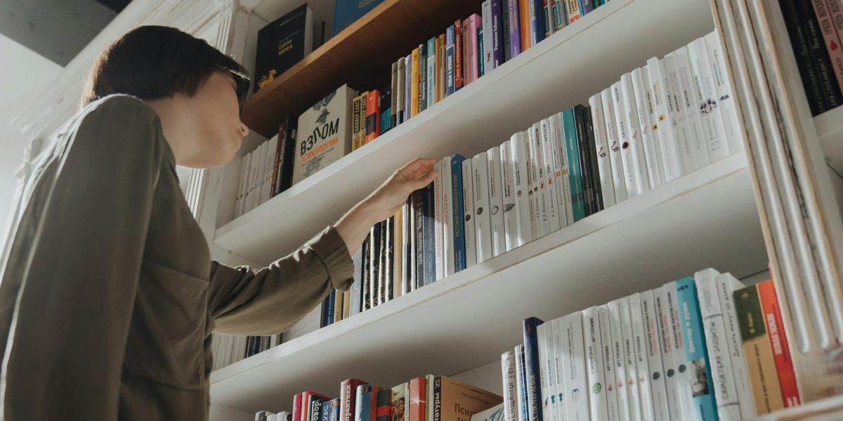 A person looking thoughtful and slightly overwhelmed by the sheer number of book options, reflecting analysis paralysis.
