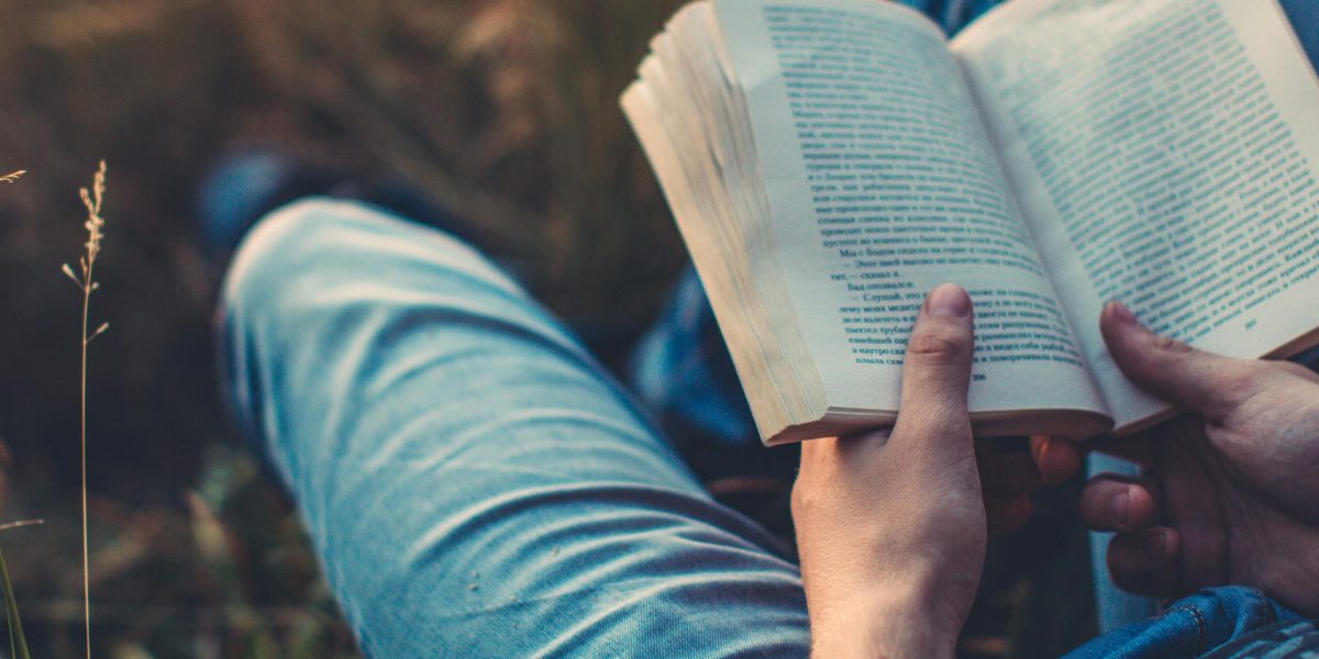 A person relaxing comfortably at home or outdoors, deeply engrossed in reading a book, enjoying a quiet moment.
