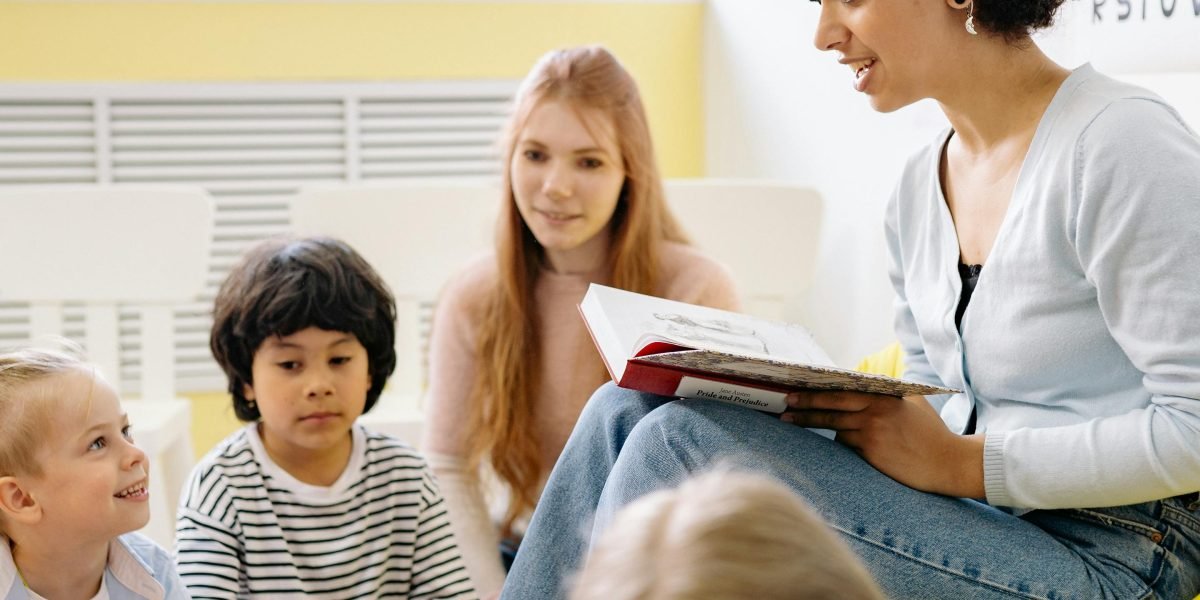 A teacher enthusiastically reading a storybook to a group of young, attentive students.