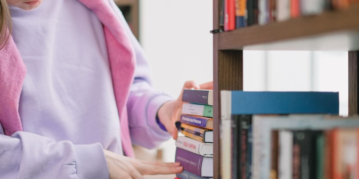 A person carefully selects a book from a well-stocked shelf, symbolizing the choice of different editions.